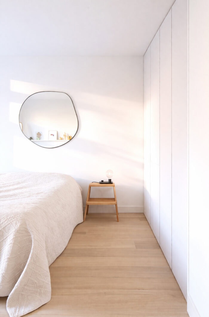 Lichte minimalistische slaapkamer met witte inbouwkast, houten nachtkastje en rond spiegel boven het bed